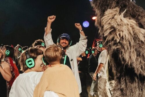 Audience with silent disco headphones gather near a puppet at The Cortège